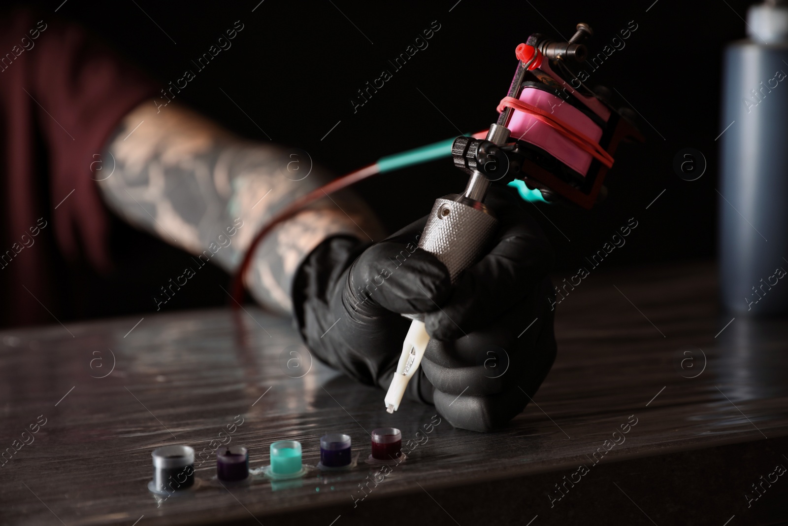 Photo of Tattoo artist with machine and ink at wooden table, closeup