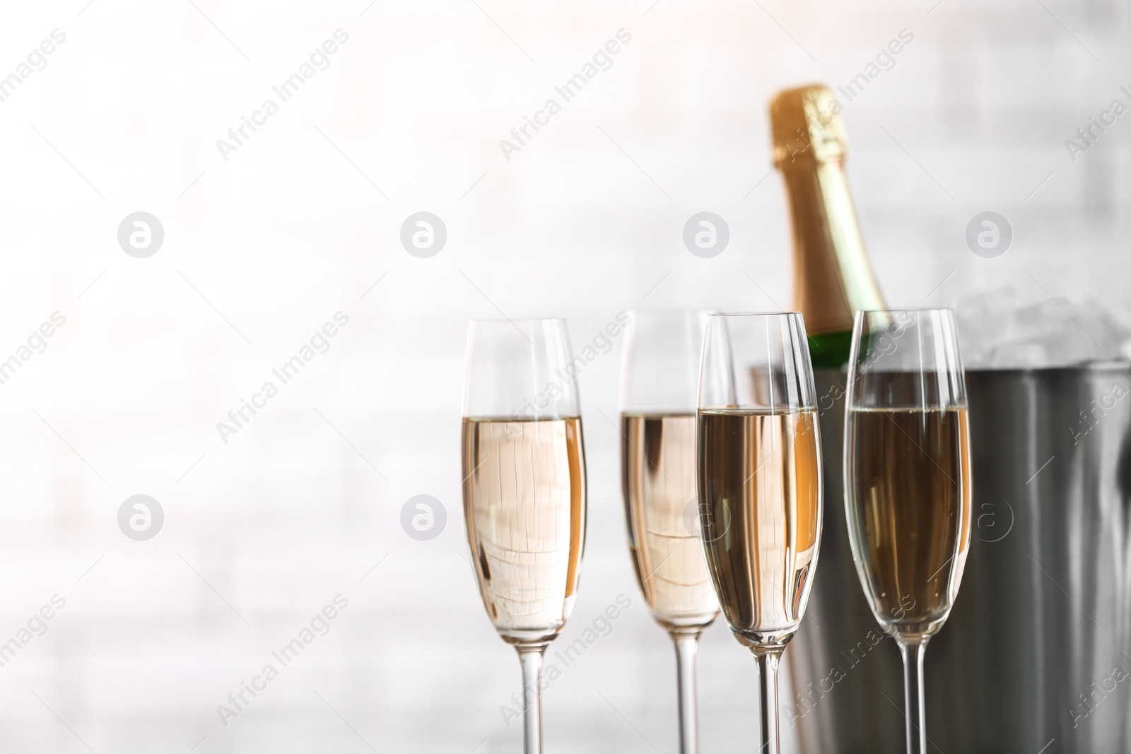 Photo of Glasses with champagne and bottle in bucket against blurred background. Celebration time