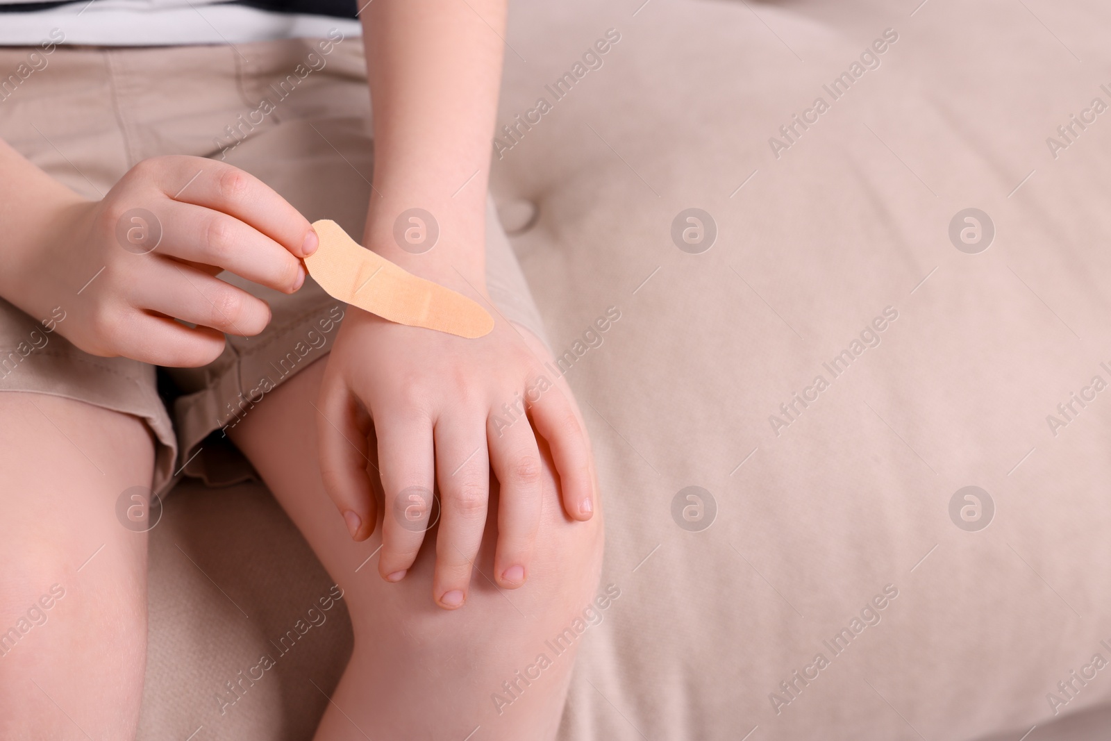 Photo of Little boy putting sticking plaster onto hand on sofa, closeup. Space for text