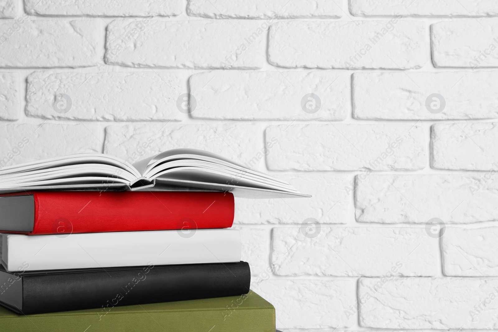 Photo of Stack of hardcover books near white brick wall, space for text