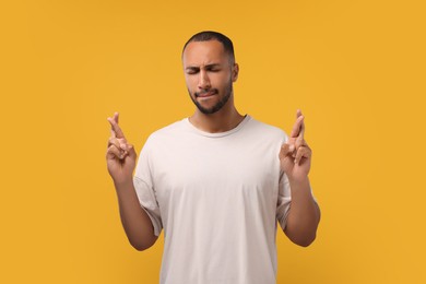 Photo of Emotional man crossing his fingers on orange background