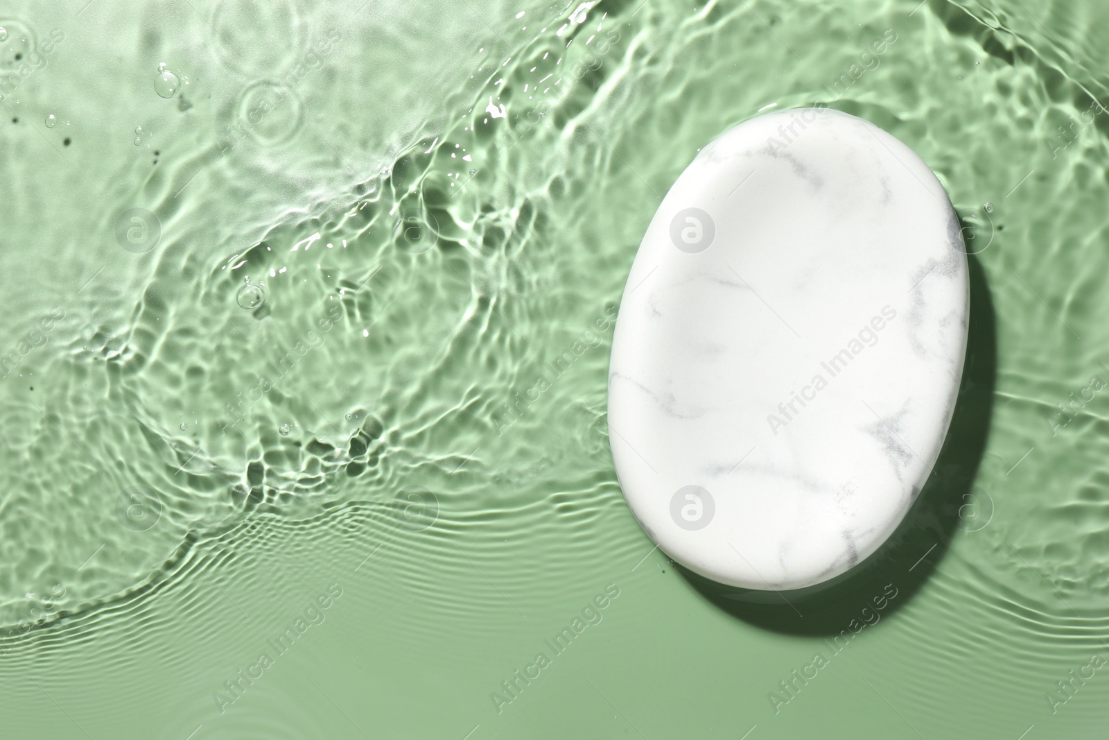 Photo of Presentation of product. Marble podium in water on green background, top view. Space for text