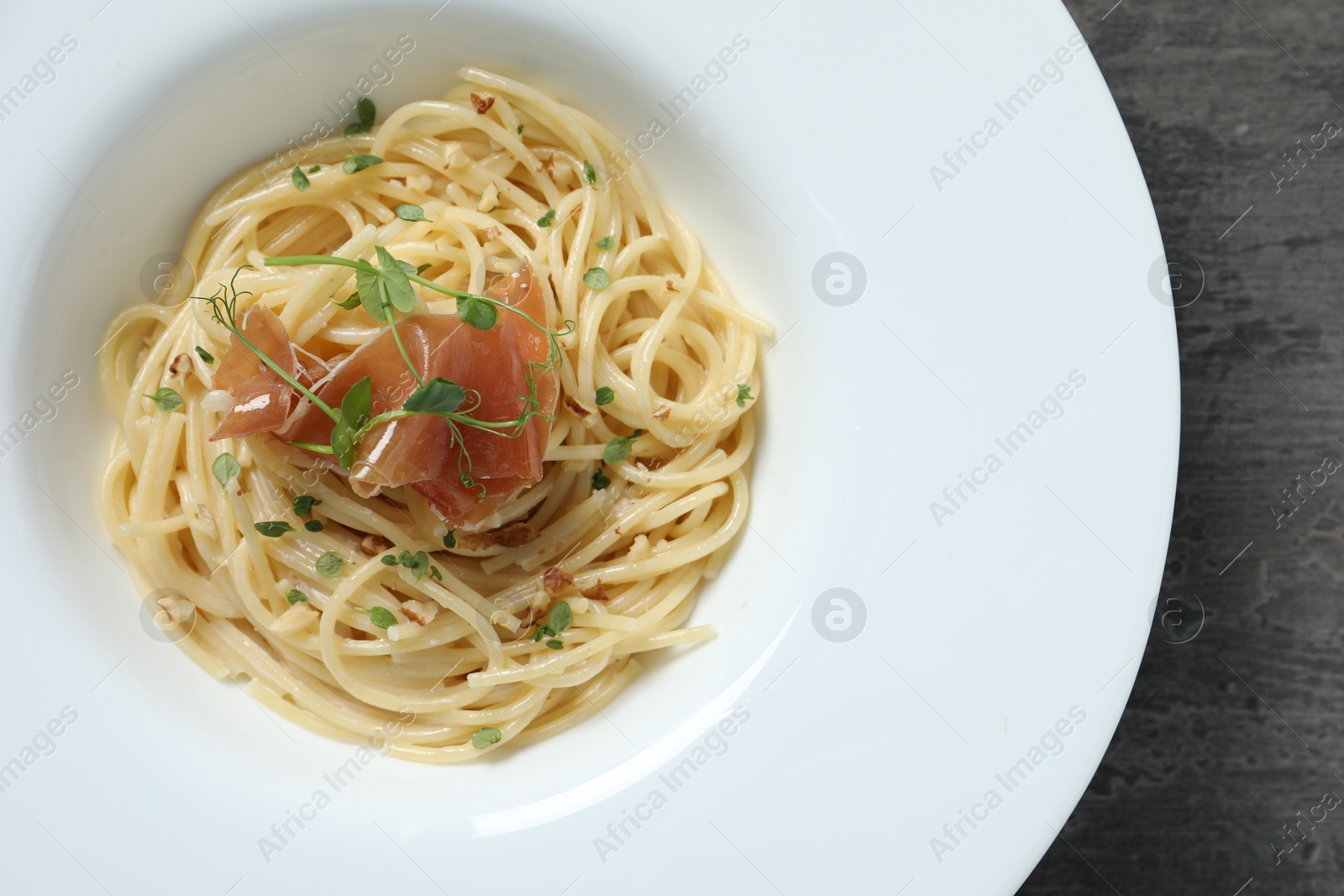 Photo of Tasty spaghetti with prosciutto and microgreens on grey textured table, top view. Exquisite presentation of pasta dish