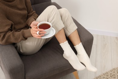 Photo of Woman in warm socks relaxing with cup of tea at home, closeup. Space for text