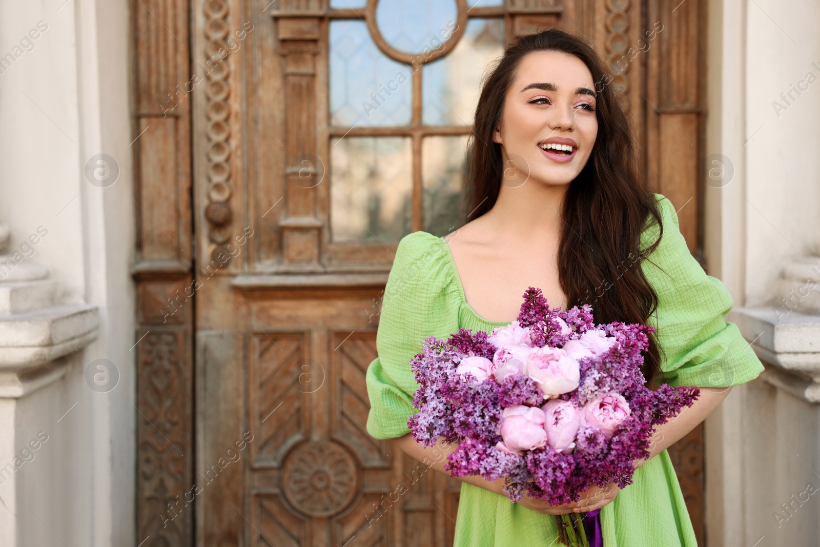 Photo of Beautiful woman with bouquet of spring flowers near building outdoors, space for text