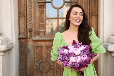 Beautiful woman with bouquet of spring flowers near building outdoors, space for text
