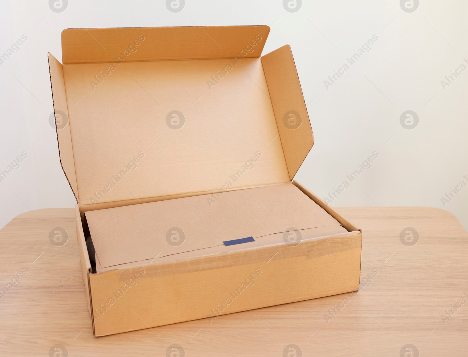 Photo of Open cardboard box with item wrapped in kraft paper on wooden table, space for text. Delivery service