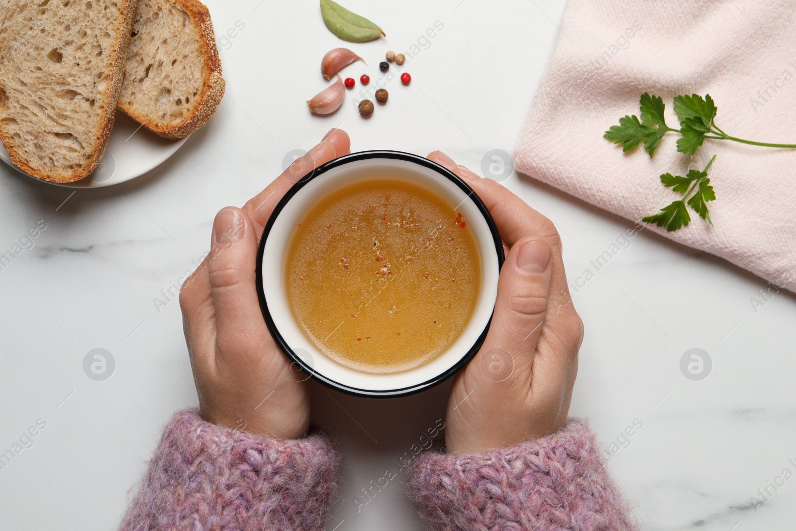 Photo of Woman with cup of hot delicious bouillon at white marble table, top view