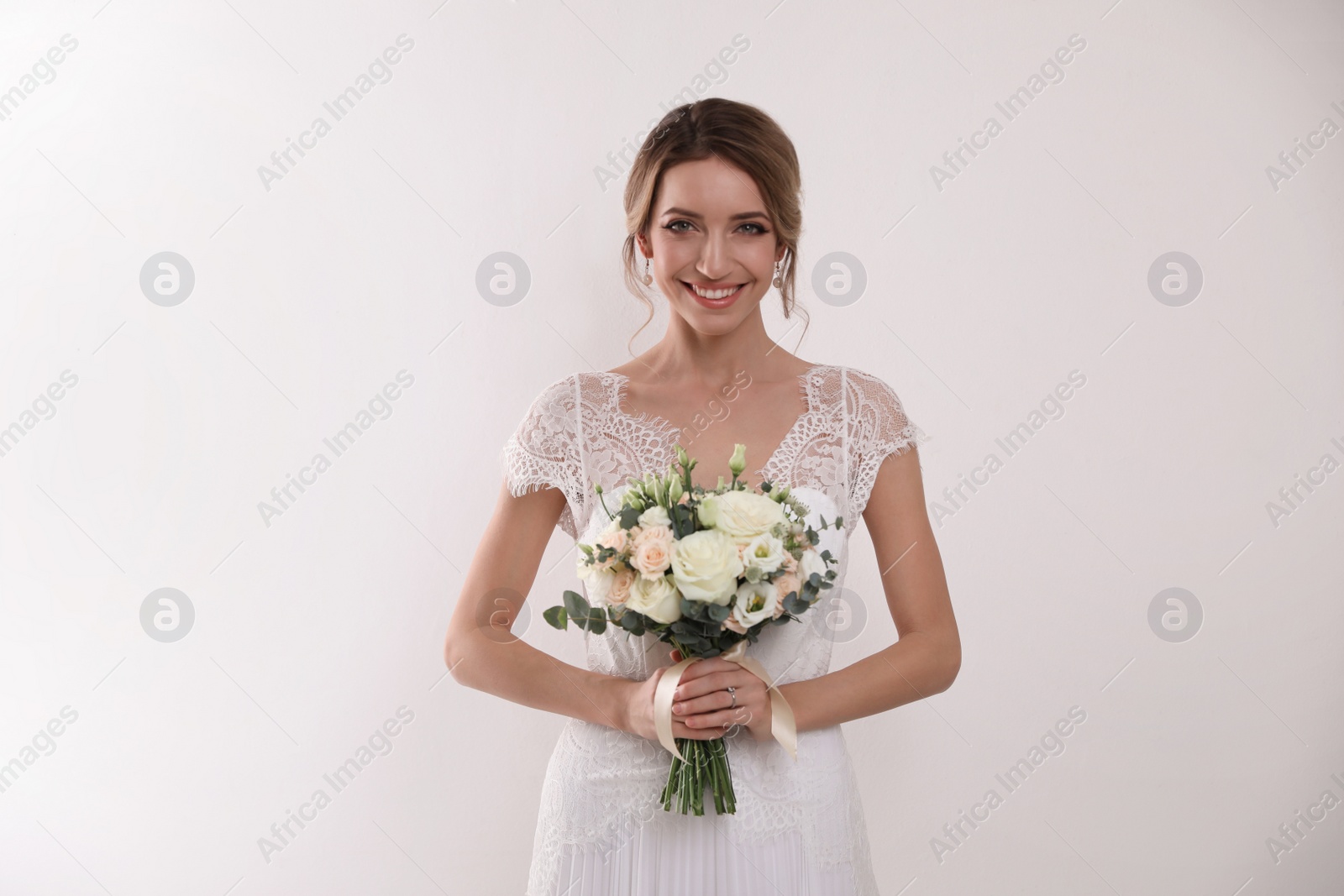 Photo of Young bride with elegant hairstyle holding wedding bouquet on white background