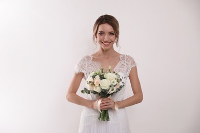 Young bride with elegant hairstyle holding wedding bouquet on white background