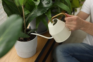 Photo of Man watering beautiful potted houseplants indoors, closeup