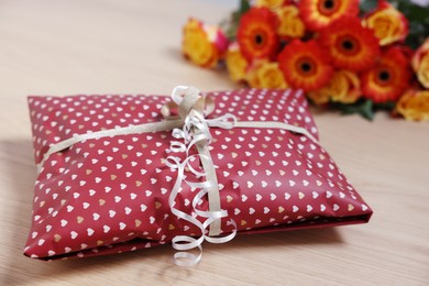 Photo of Parcel wrapped in heart patterned paper and beautiful flowers on wooden table, closeup