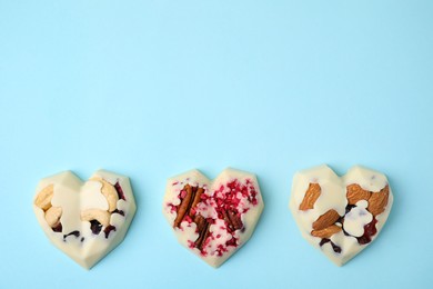 Photo of Tasty chocolate heart shaped candies with nuts on light blue background, flat lay. Space for text