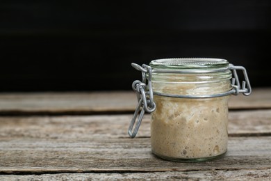 Photo of Leaven in glass jar on wooden table, space for text