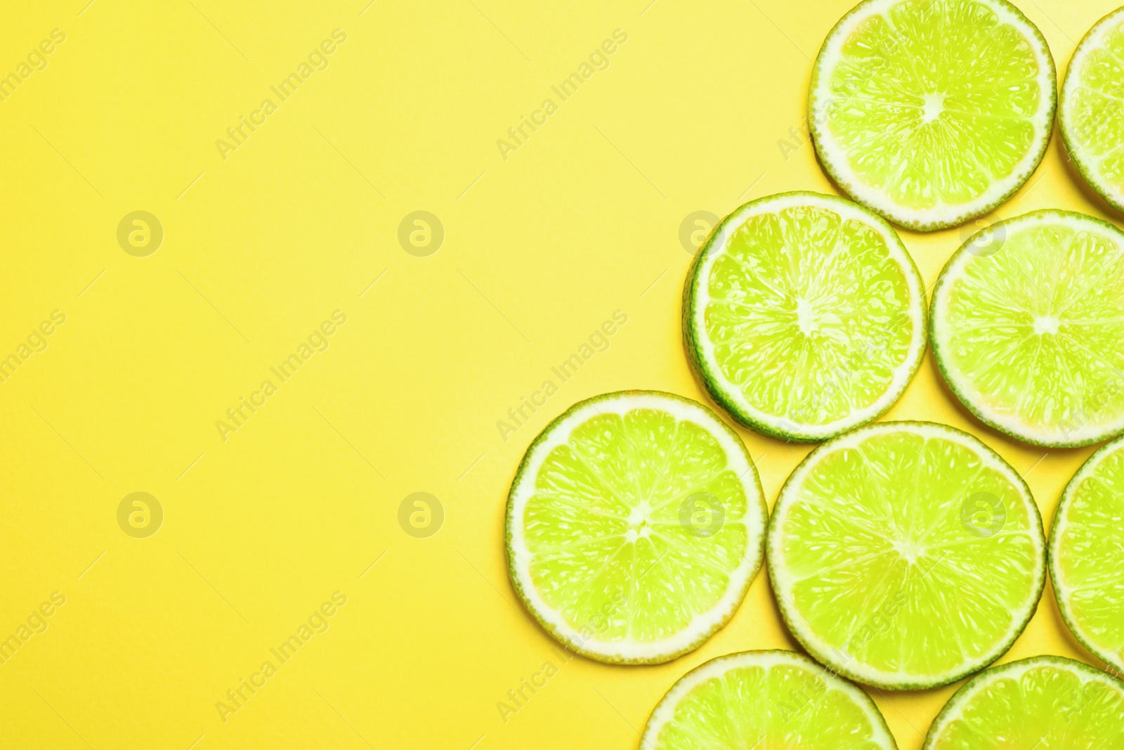 Photo of Juicy fresh lime slices on yellow background, flat lay. Space for text