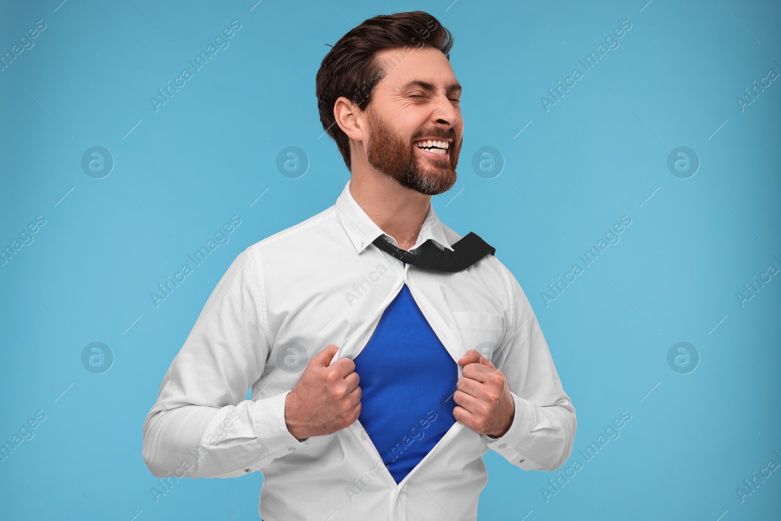 Photo of Happy businessman wearing superhero costume under suit on light blue background