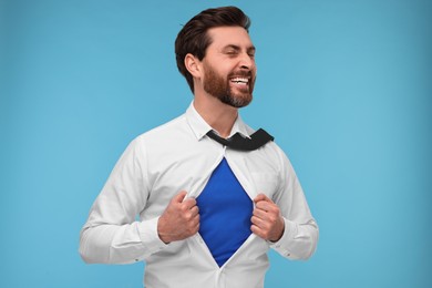 Happy businessman wearing superhero costume under suit on light blue background