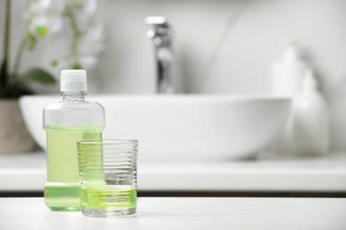 Bottle and glass with mouthwash on white countertop. Space for text