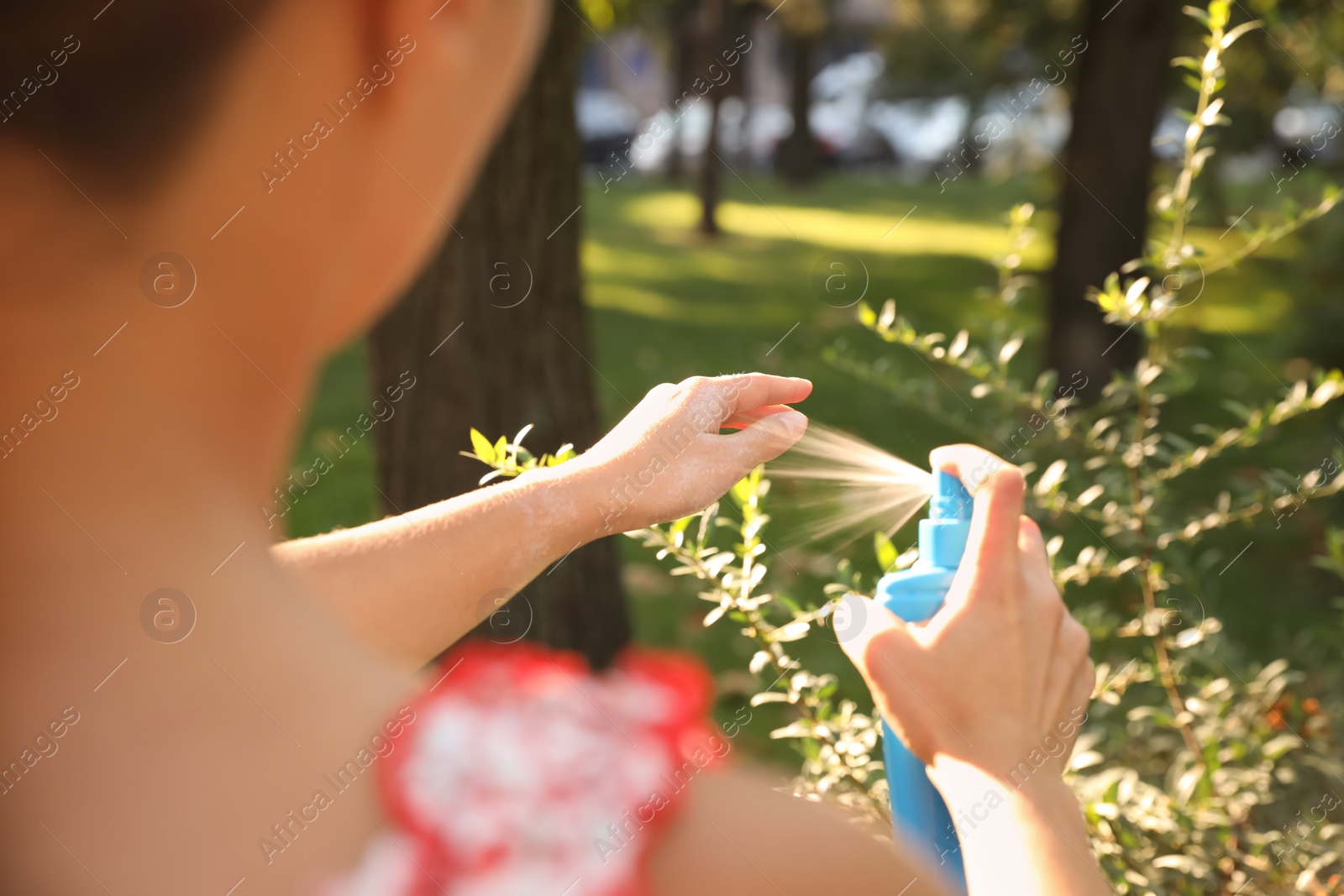 Photo of Woman applying insect repellent onto hand in park, closeup