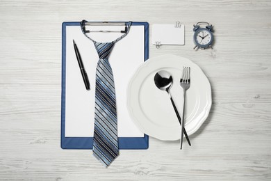 Photo of Plate with cutlery, tie, clipboard and alarm clock on wooden table, flat lay. Business lunch concept