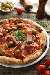 Photo of Tasty pizza with cured ham, olives, tomatoes and parsley on wooden table