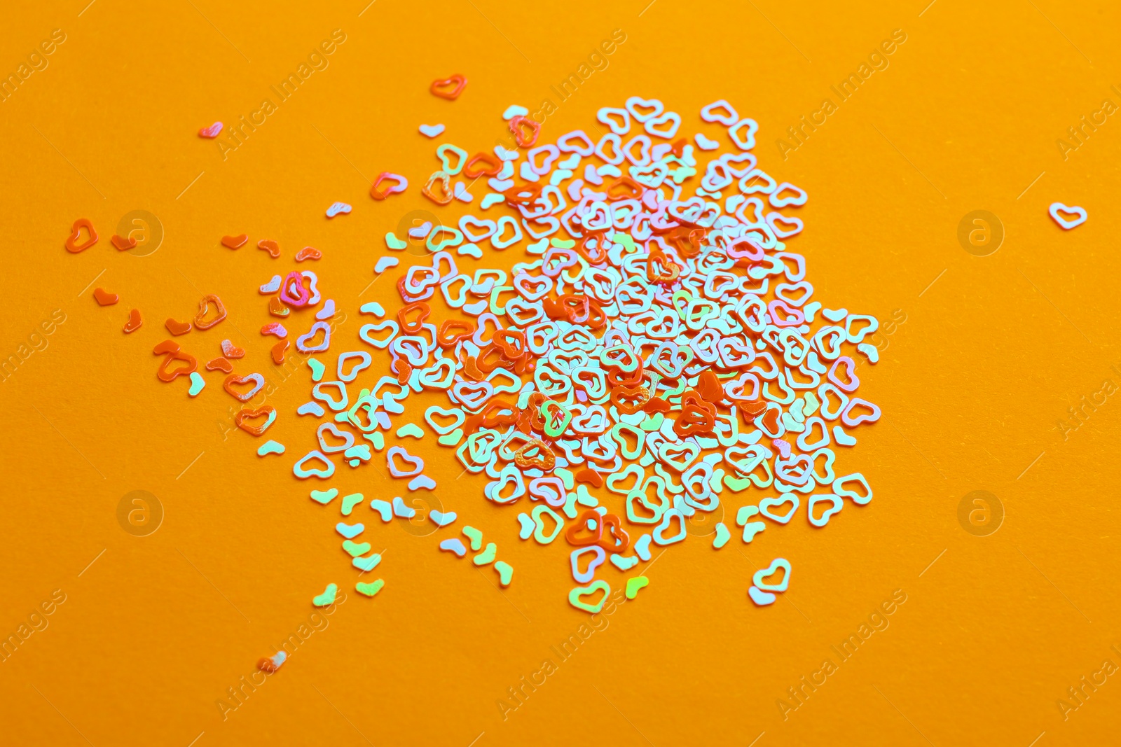 Photo of Shiny bright heart shaped glitter on pale orange background