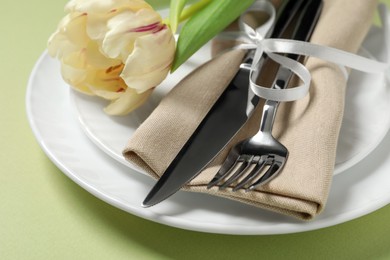 Stylish table setting with cutlery and tulip on light green background, closeup
