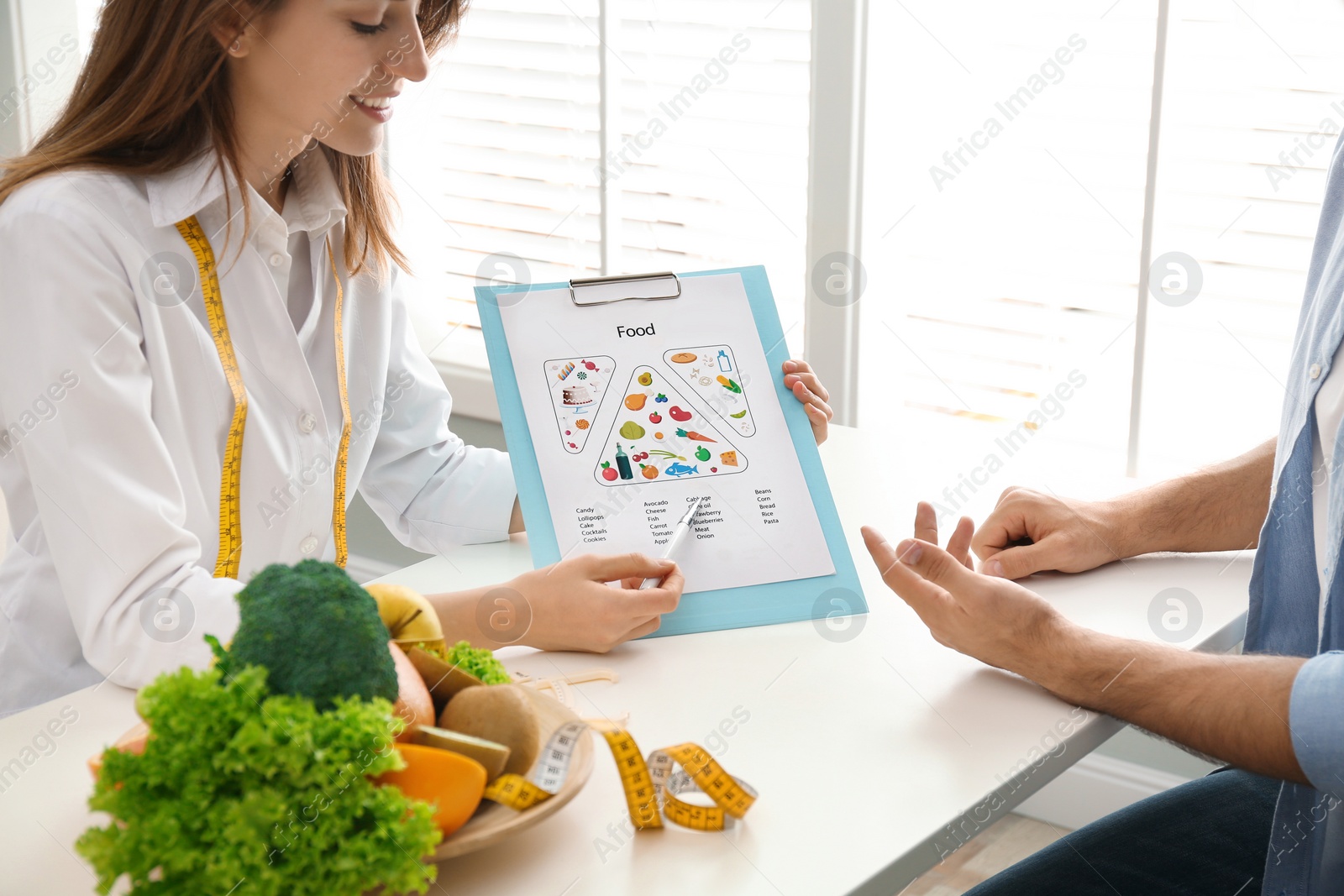 Photo of Young nutritionist consulting patient at table in clinic, closeup