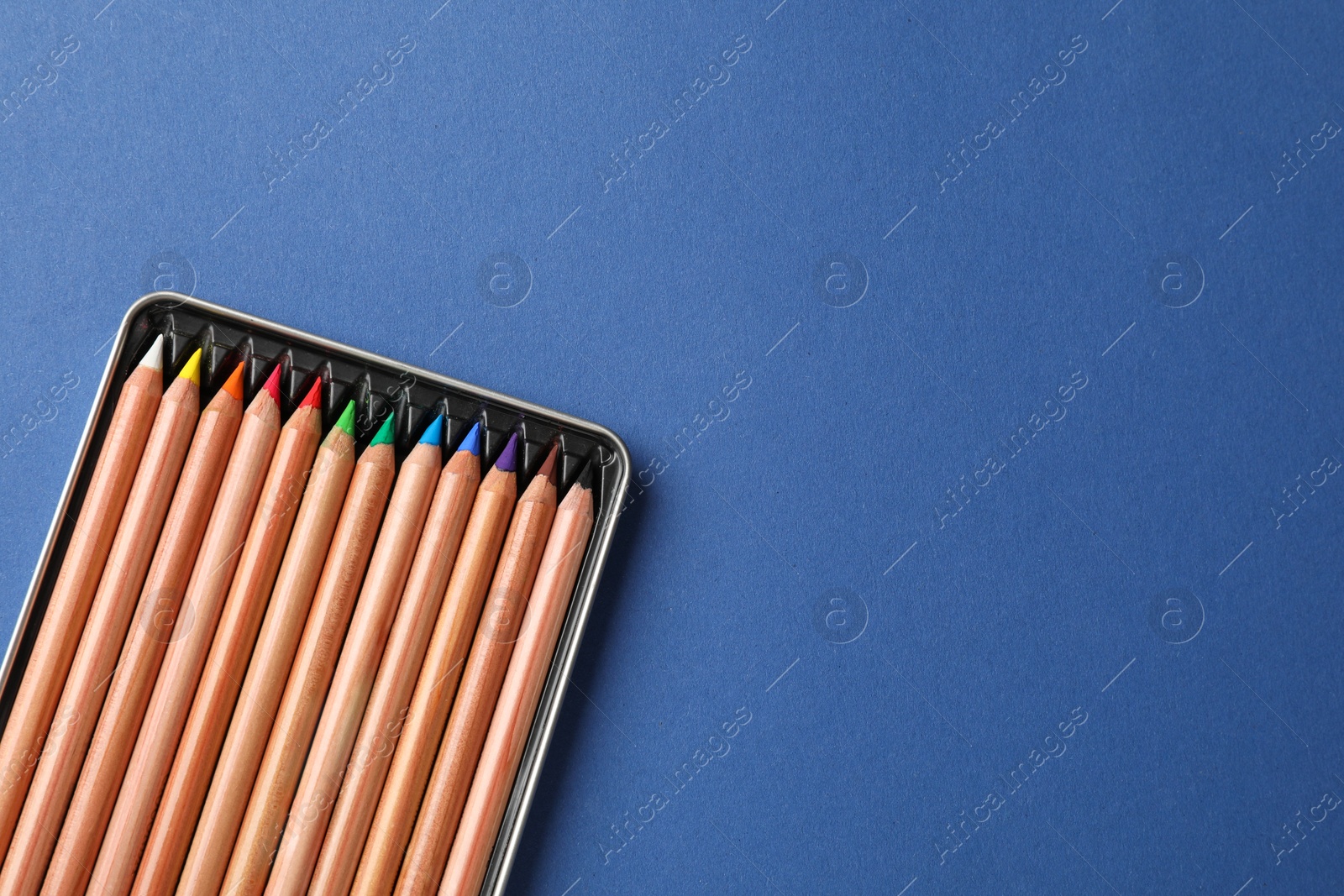 Photo of Box with many colorful pastel pencils on blue background, top view and space for text. Drawing supplies