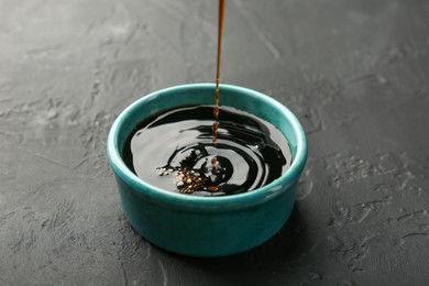 Photo of Pouring tasty soy sauce into bowl on black table, closeup