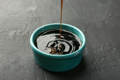 Pouring tasty soy sauce into bowl on black table, closeup