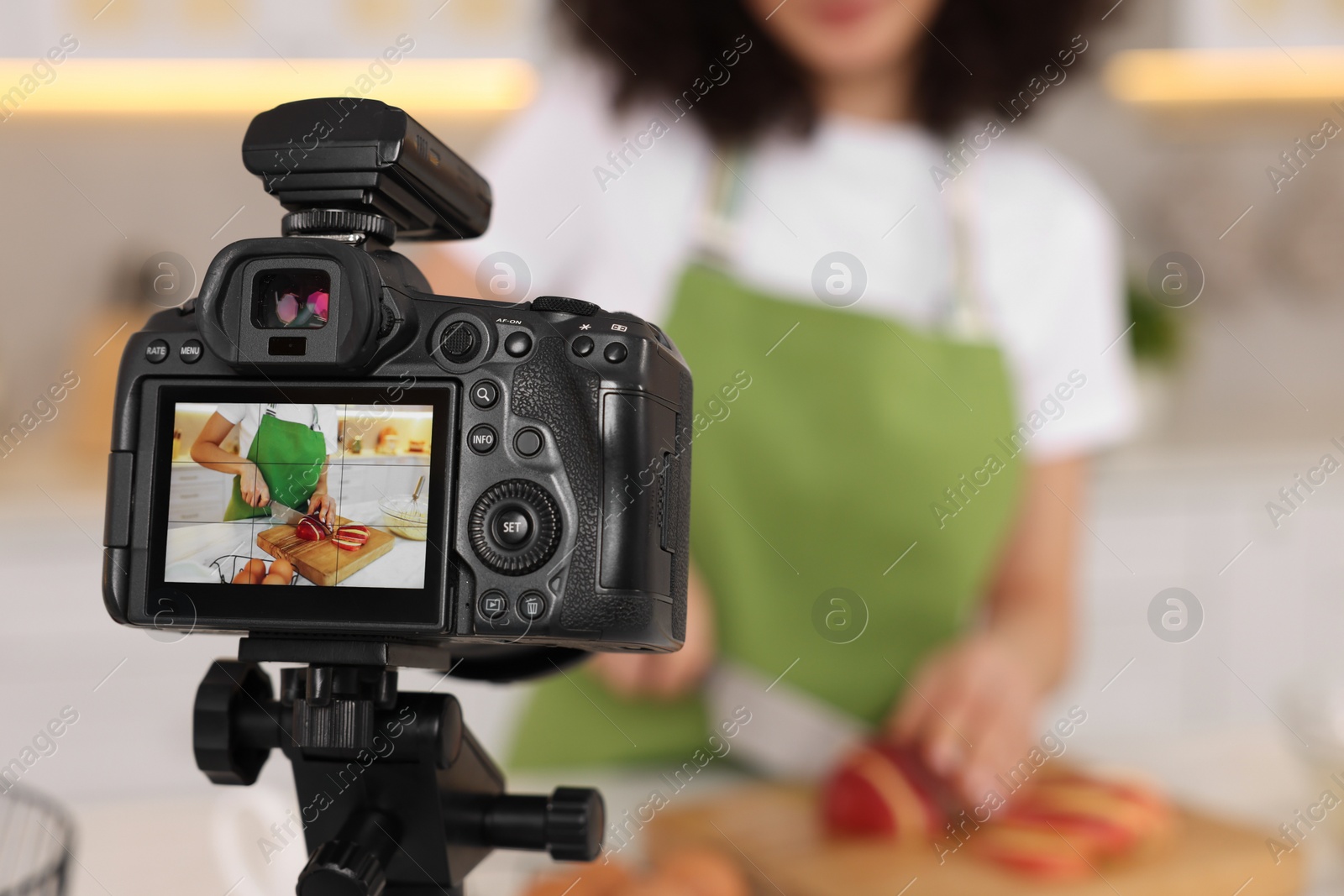 Photo of Food blogger cooking while recording video in kitchen, focus on camera