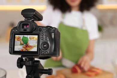 Photo of Food blogger cooking while recording video in kitchen, focus on camera