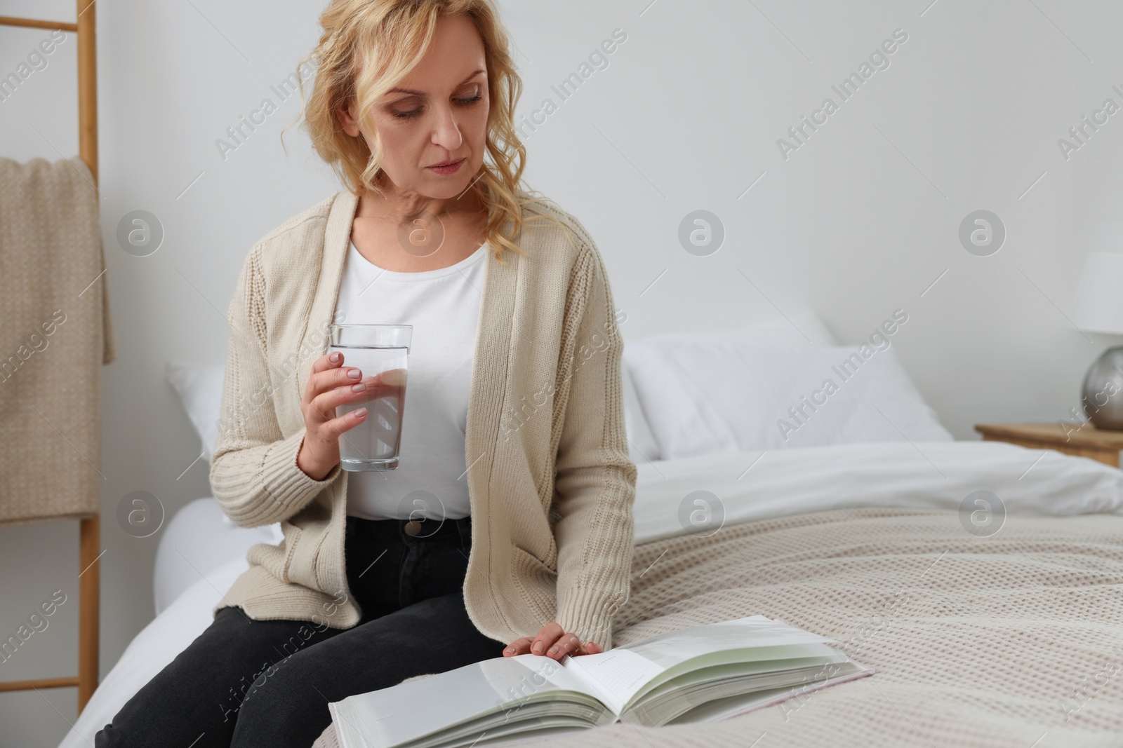 Photo of Upset middle aged woman with book and glass of water at home. Loneliness concept