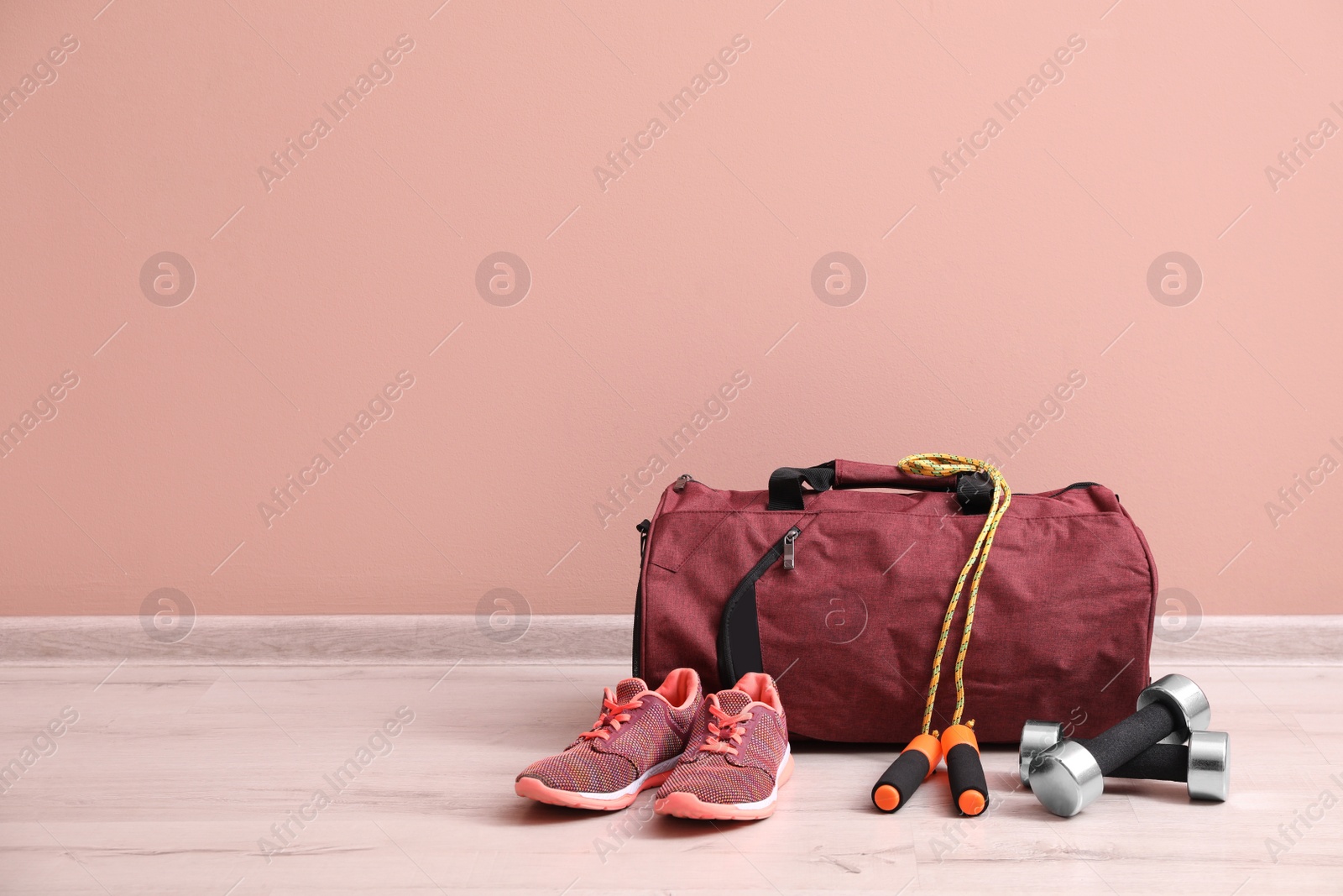 Photo of Red bag and sports accessories on floor near pink wall, space for text