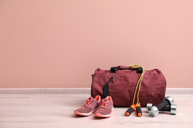 Red bag and sports accessories on floor near pink wall, space for text