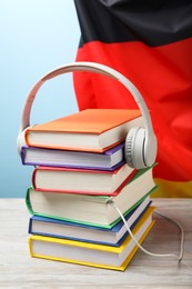 Learning foreign language. Different books and headphones on wooden table near flag of Germany