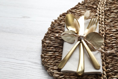 Photo of Cutlery and wicker mat on white wooden background, space for text. Autumn table setting