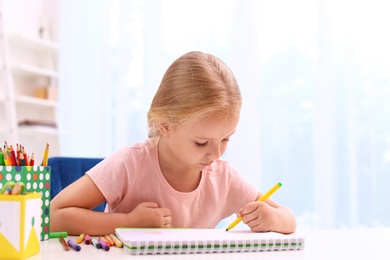 Cute little left-handed girl drawing at table in room