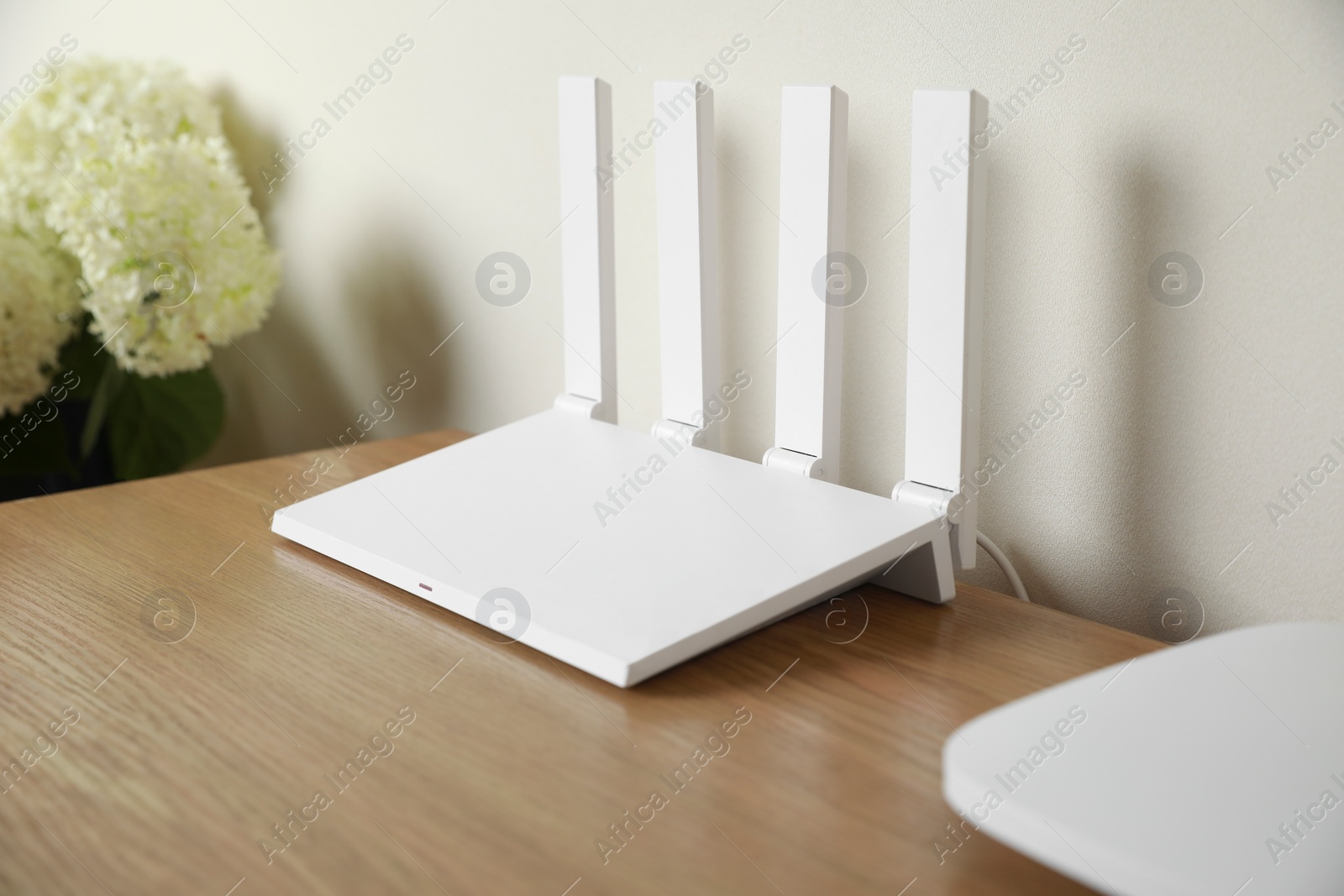 Photo of New modern Wi-Fi router on wooden table near white wall