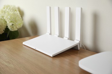 New modern Wi-Fi router on wooden table near white wall