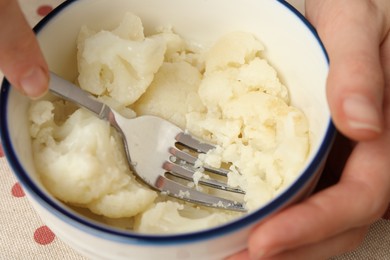 Photo of Woman making baby food with cauliflower at table, closeup