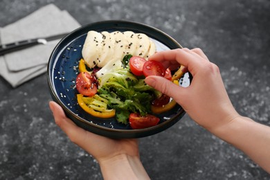 Photo of Food stylist preparing delicious salad with mozzarella and tomatoes for photoshoot at dark grey table in studio, closeup