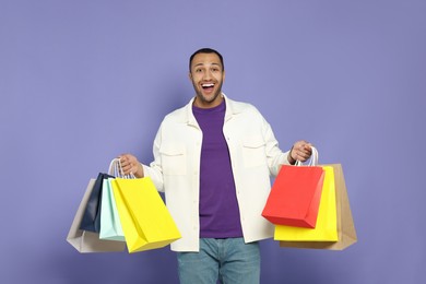 Photo of Happy African American man with shopping bags on purple background