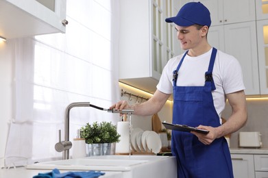 Smiling plumber with clipboard examining faucet in kitchen