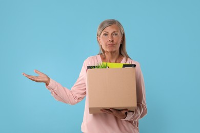 Photo of Confused unemployed senior woman with box of personal office belongings on light blue background