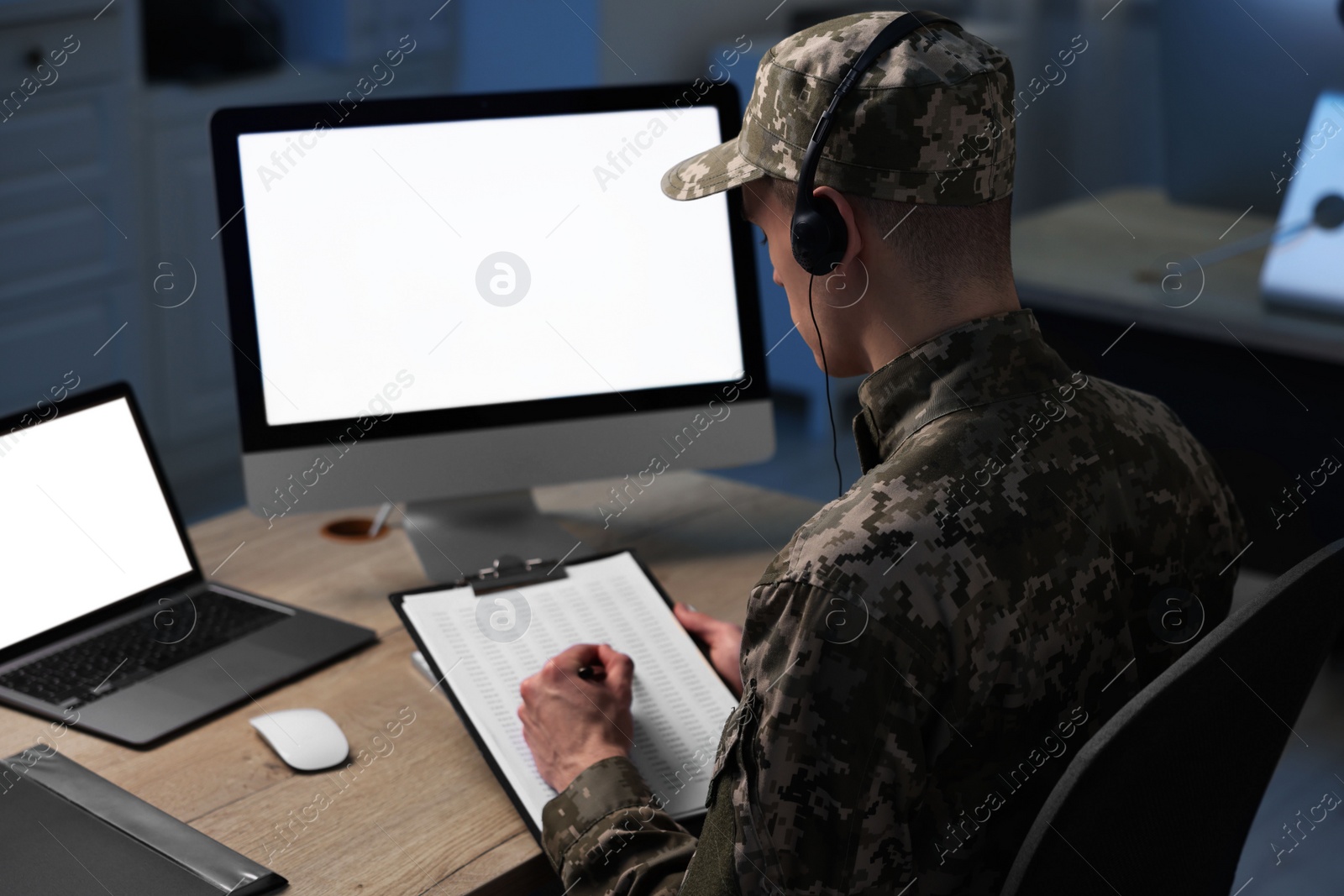 Photo of Military service. Soldier with clipboard and headphones working at table in office