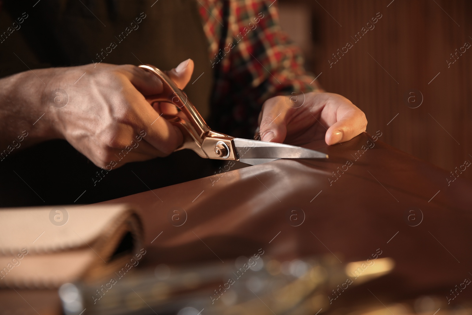 Photo of Man cutting leather with scissors in workshop, closeup