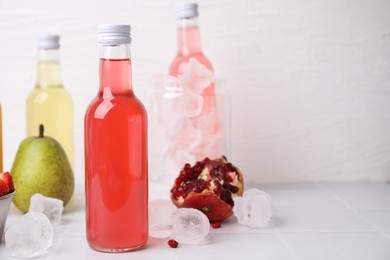 Photo of Tasty kombucha in glass bottles, fresh fruits and ice on white table, space for text