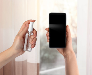 Woman sanitizing smartphone with antiseptic spray indoors, closeup. Be safety during coronavirus outbreak 